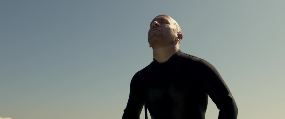 Bald man sitting over a white surfboard floating on the ocean