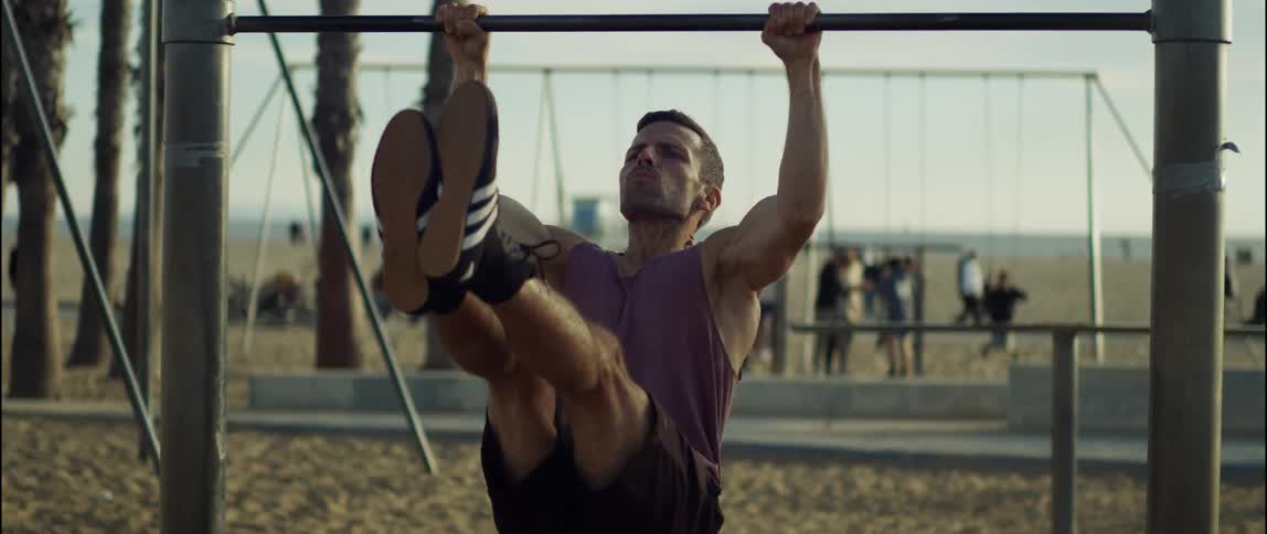 Man exercises at park on the beach as other people move around in the background