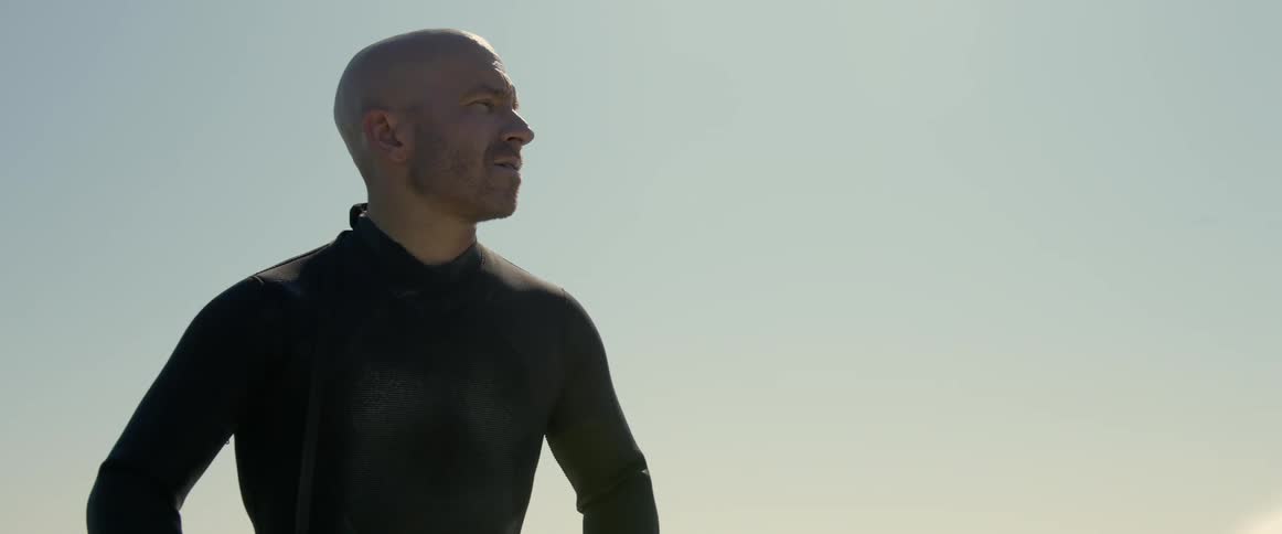 An older white man is surfing on the ocean in the middle of the day