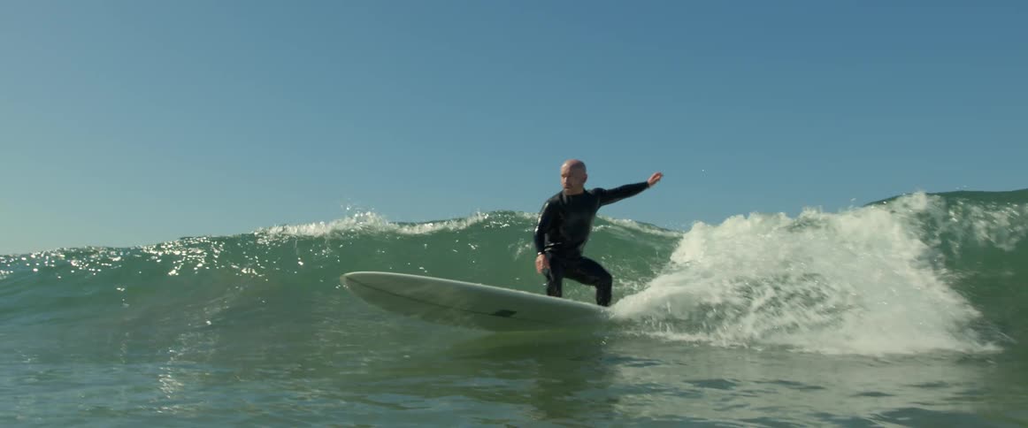 Male surfer wearing wet suit rides wave under a clear sky