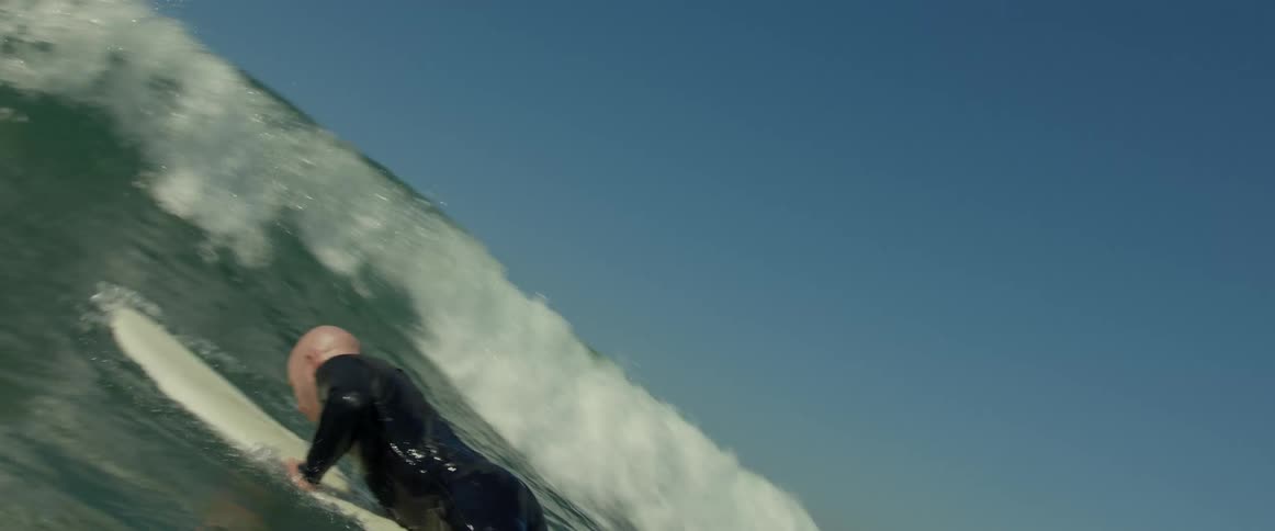 A large waves goes over a man as he paddles his surfboard out in the ocean