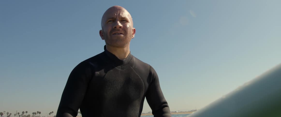 Bald man sitting on a white surfboard floating on the ocean