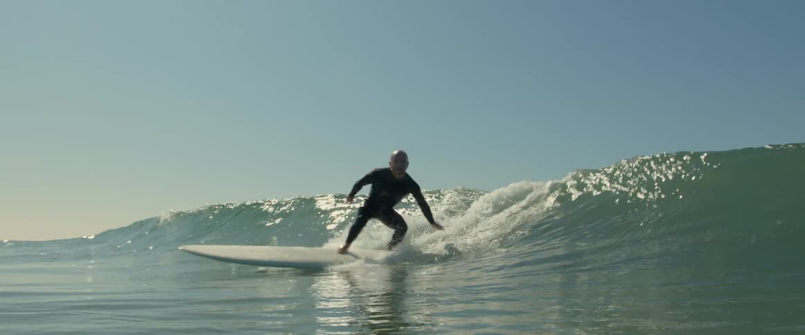 A man in a wet suit surfs in front of a wave on the ocean during the day