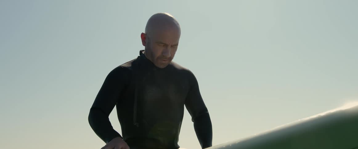 Bald man sitting over a white surfboard floating on the ocean