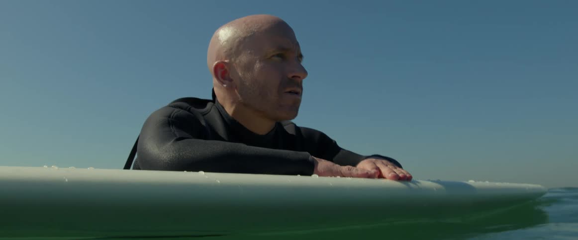 A man in the ocean leans on his surfboard and looks around