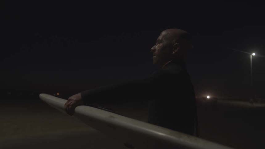 A man holding a surfboard is walking near a road at night