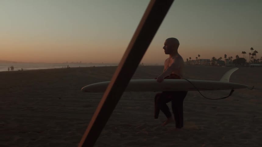 A man carries his surf board across the beach to the water