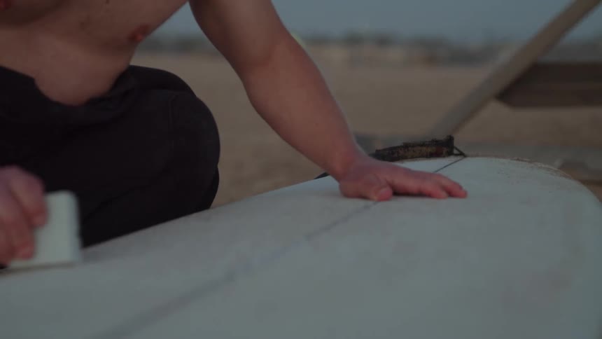A man is cleaning his surf board on the beach