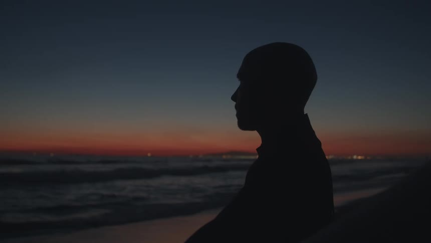 Silhouette of a man standing on a beach in front of the ocean at sunset