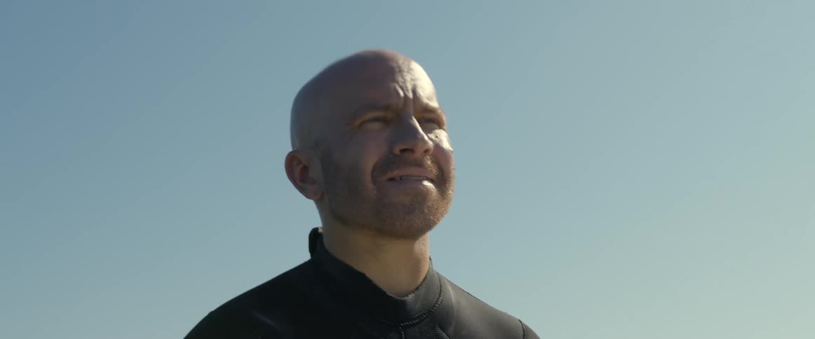 A man sitting on his surfboard squinting as he look out at the ocean