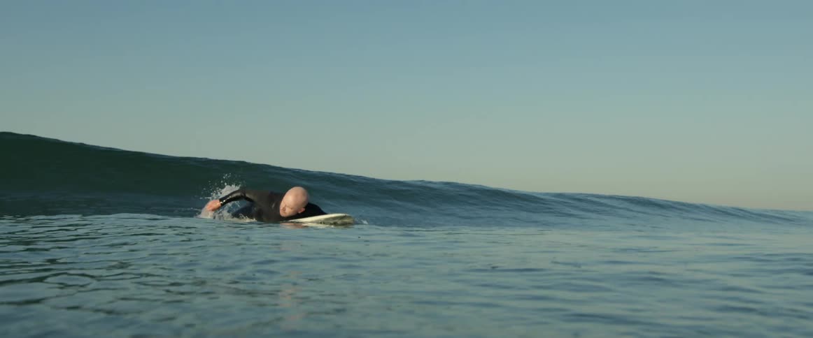 A surfer paddles with his arms while lying atop a surfboard on the ocean during the day