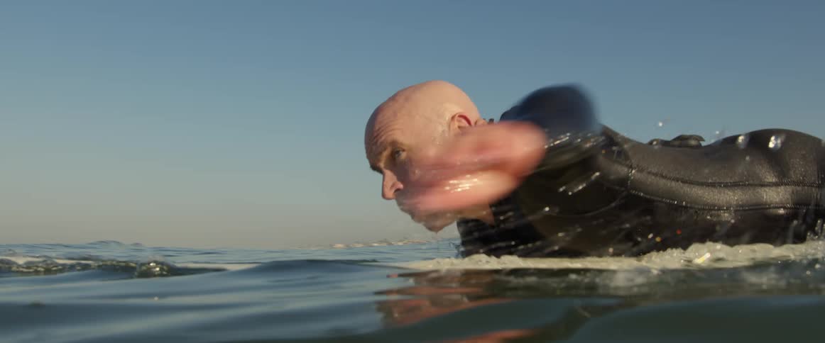 An older man is surfing on the ocean in the middle of the day