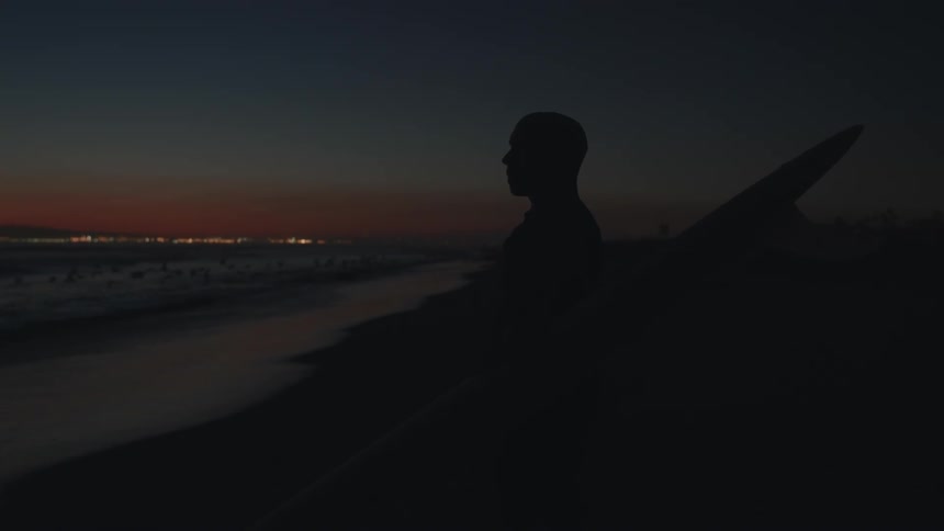 A man looks out over the ocean while standing on a beach at night