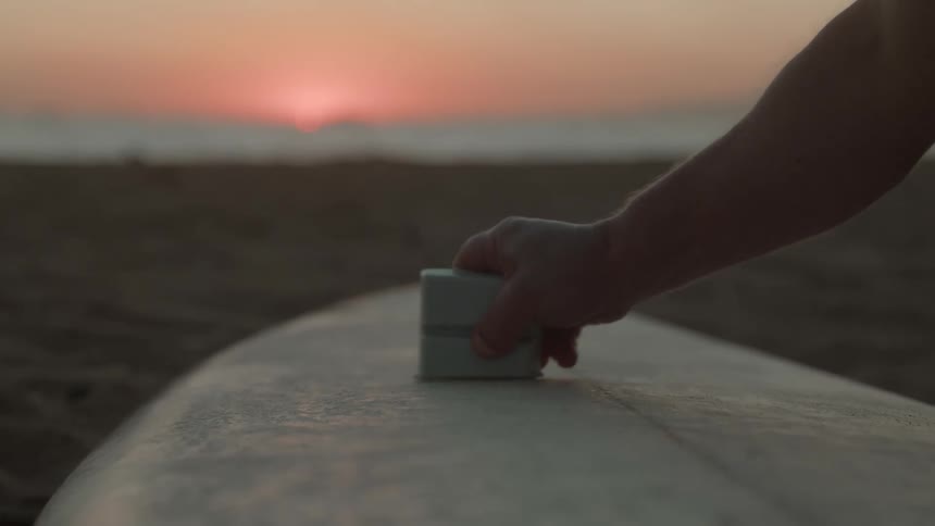 A man waxes his surfboard on the beach