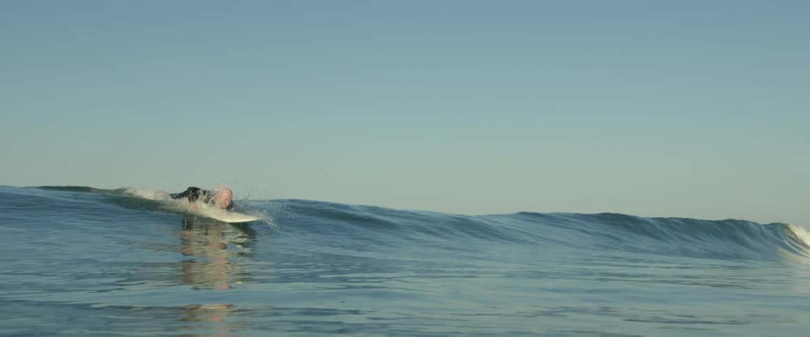 An older white man is surfing outdoors on an ocean