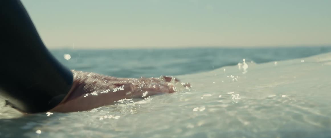 A man is in the water moving his hands across his surfboard