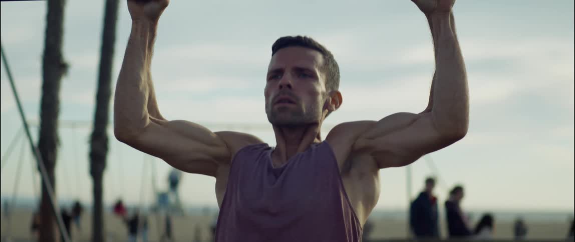 A man is outside doing pull ups on a metal bar in a park
