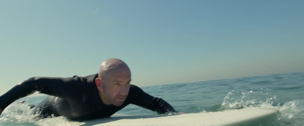 An older white man is surfing outside in the ocean
