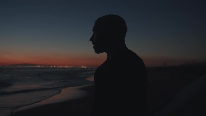 Silhouette of a man carrying a surfboard on a beach in front of the ocean at sunset