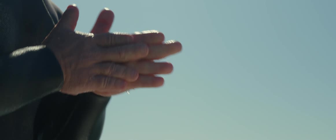A surfer rubs his hands together before lying down on a surfboard