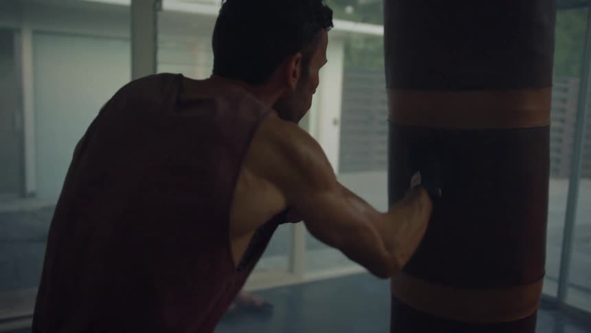 A man trains by striking a punching bag indoors during the day