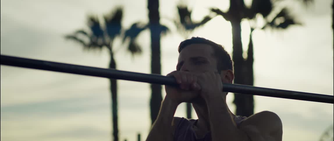 A man does pull ups on a bar outdoors during the day