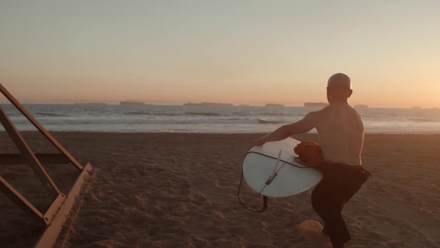 A man carries his surfboard closer to the ocean and sets it down