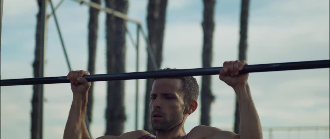 Young strong man doing pull ups on a public park on the beach at morning