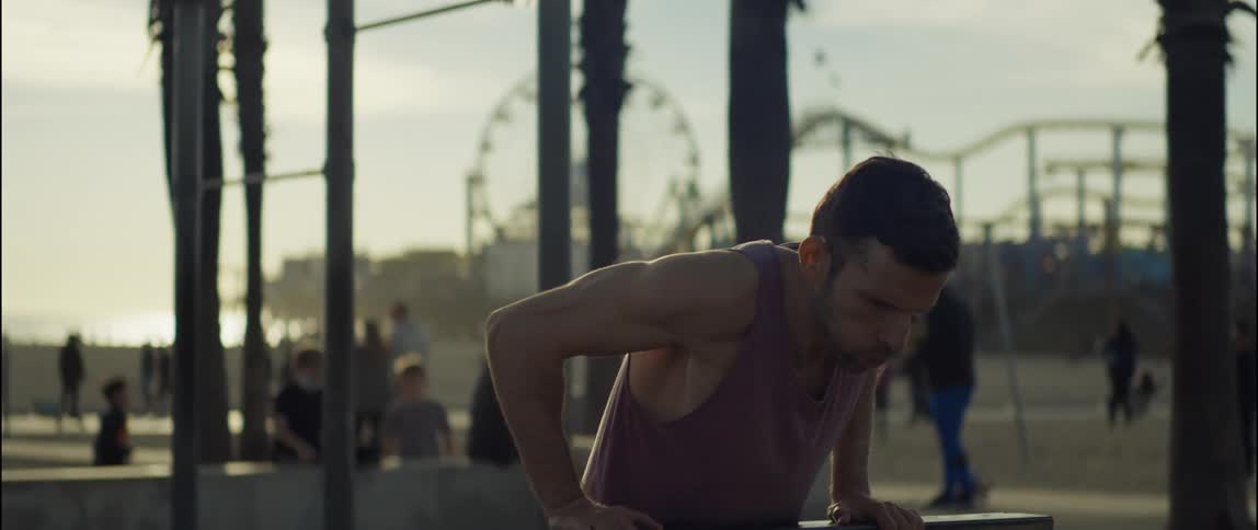 Man exercises at park at the beach with amusement park and others in the background