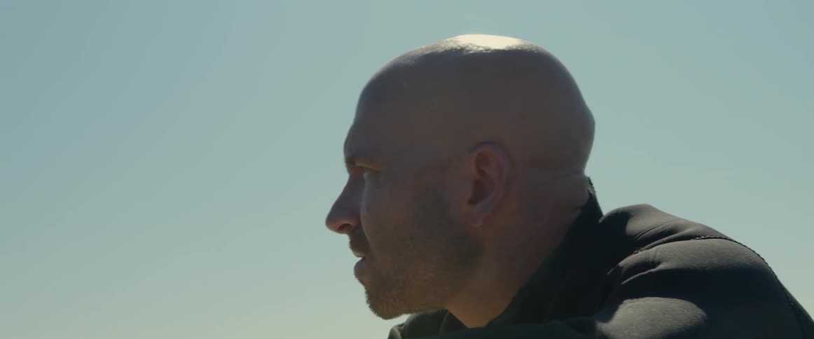 A man in the ocean leans on his surfboard and looks in to the distance