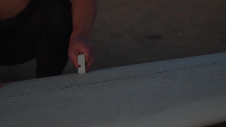 A woman is waxing a surfboard