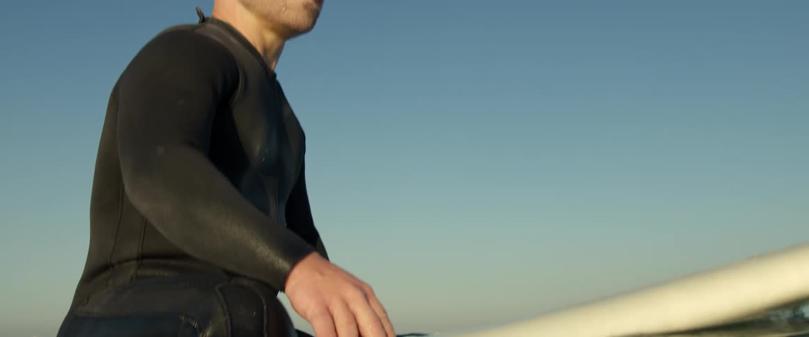 Man wearing wet suit sits on surfboard in the ocean
