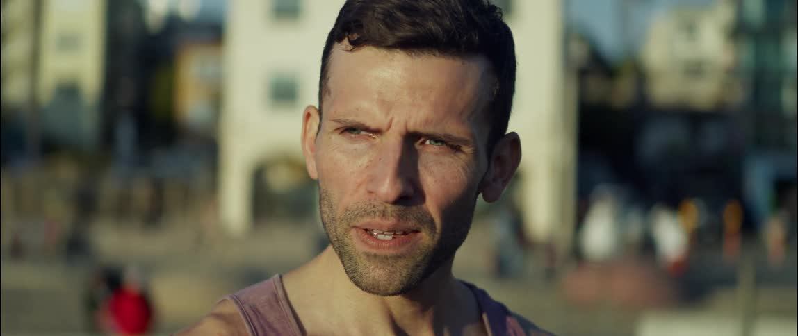 A man in a tank top squinting outside on a sunny day