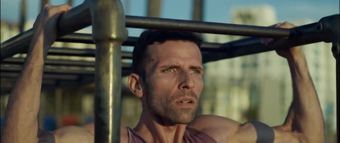 Man exercises using the monkey bars with buildings in the background