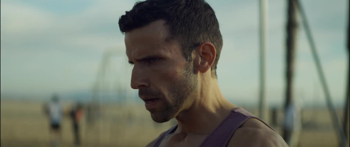 A man catches his breath while standing amongst exercise equipment on a beach during the day