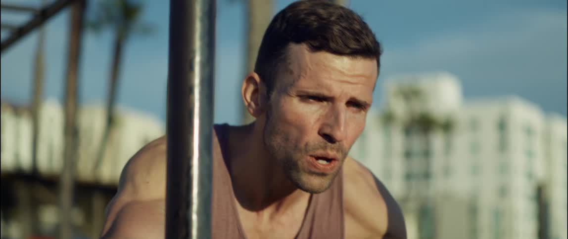 A man exhales and strains as he does push ups on a bar in a park