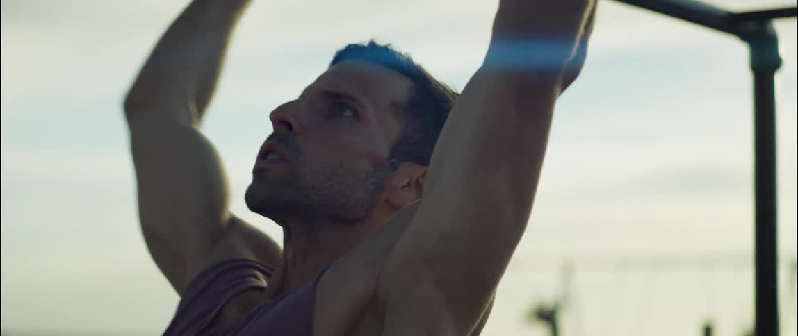 A man is working out on some bars while another man swings
