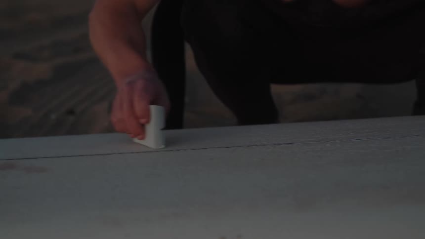A man waxes his surfboard on the beach