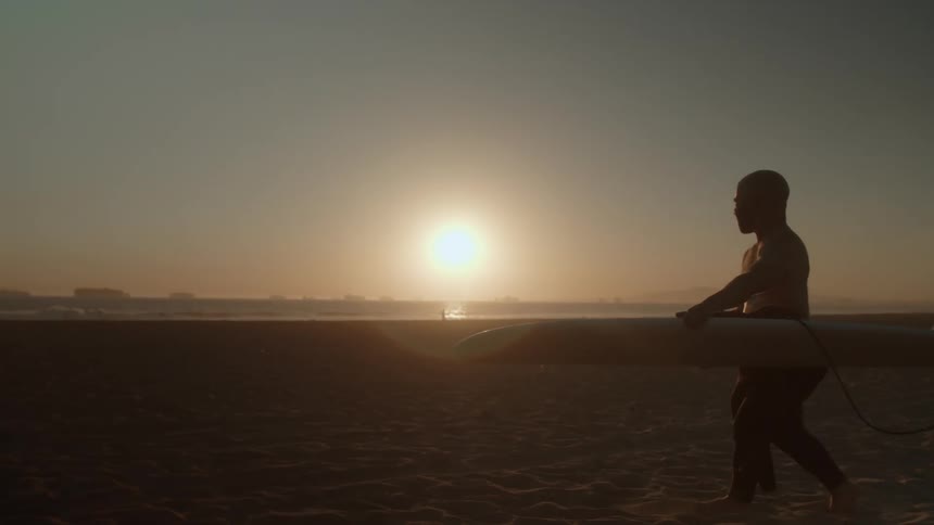 A man carries his surfboard across the beach