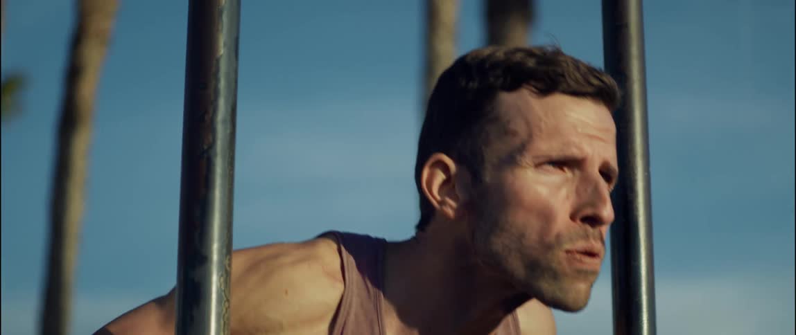 The sun shines on the face of a man outside doing exercises near metal bars