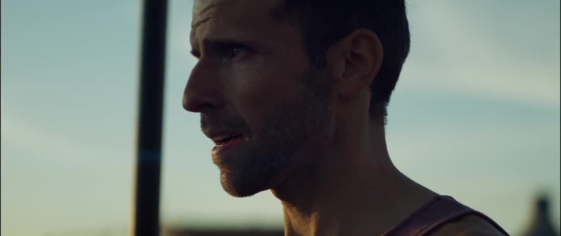 The sun shines on the face of a man standing outside and there are palm trees in the distance