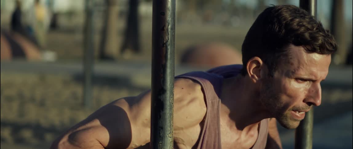 A man uses bars at a beach side park to do push ups straining and sweating