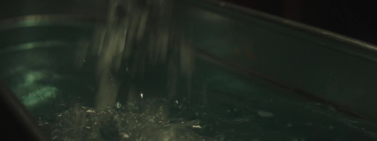A man is dumping a bag of ice into a metal tub