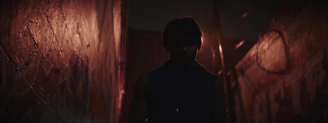 A silhouetted man backlit by a street lamp in an alley at night