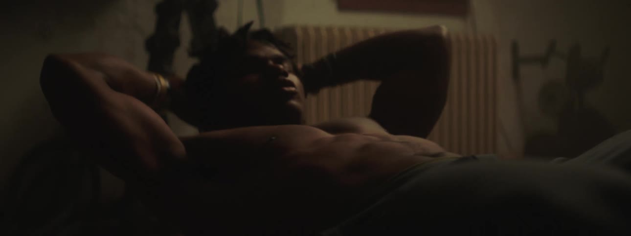 A shirtless man does sit ups indoors