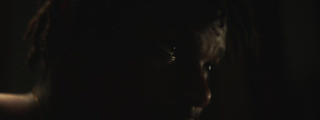 A young black person is sitting down in the dark