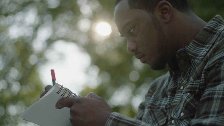 A man writes while sitting in the woods