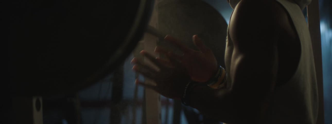 Young man powders his hands to lift weights inside a dimly lit gym