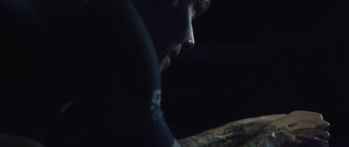 Focused sweaty man wearing a cycling jersey exercising on a stationary bike in a dark room