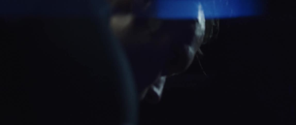 Focused cyclist man wearing a cycling jersey holding a bottle of water and exercising on a stationary bike on a dark room